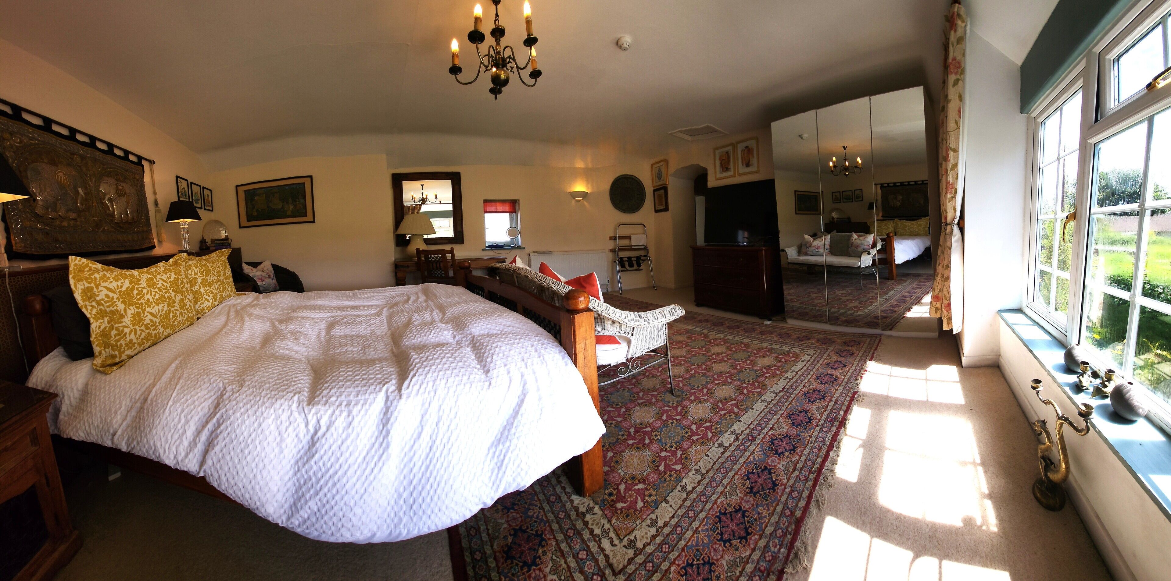 Une chambre dotée d’un grand lit, d’un coin salon avec un fauteuil, d’une télévision et offrant une vue sur le jardin par la fenêtre.