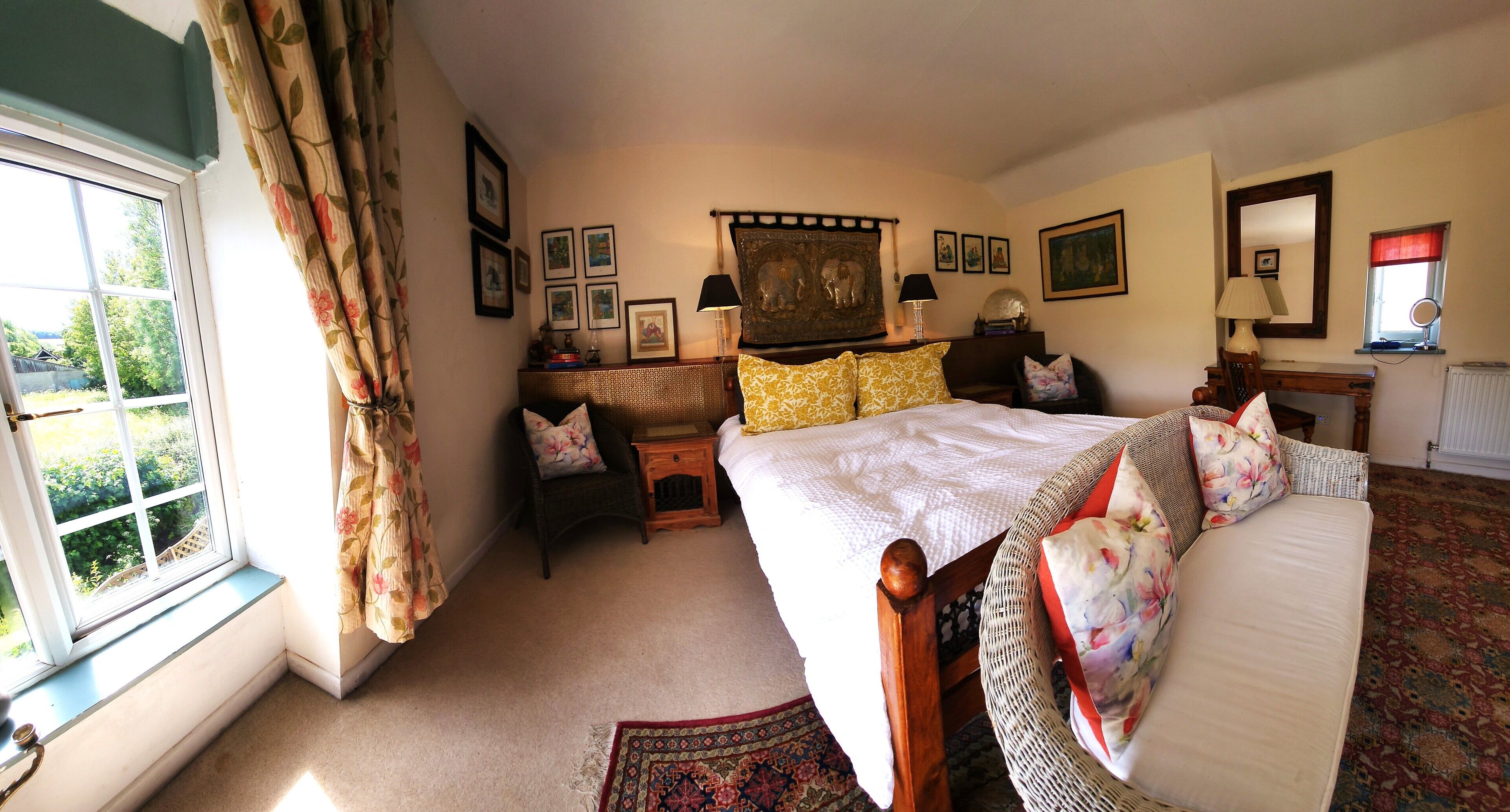 A bedroom with a bed, a chair, a table, a window with curtains, and wall-mounted lamps.