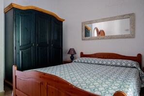 A bedroom with a wooden bed, a dark wardrobe, a bedside lamp, and a mirror on the wall. - ISOLA ALTA - BUDONI SWEET HOME (Porto Ottiolu)