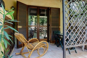 A room with a wicker rocking chair, a table, and a lattice screen. - ISOLA ALTA - BUDONI SWEET HOME (Porto Ottiolu)