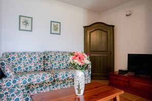Ein Wohnzimmer mit einem gemusterten Sofa, einem Holztisch, einem Fernseher auf einer Holzkommode und einer Tür im Hintergrund.