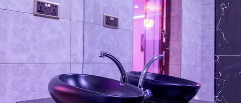 Un baño moderno con dos lavamanos negros tipo recipiente, una salpicadura de mármol y un espejo que refleja el interior.