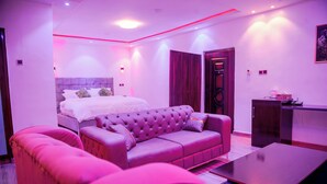 A modern bedroom with a bed, a pink sofa, a coffee table, and a desk. - Aureza Paradise Hotel (Tamale)