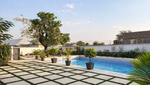 A swimming pool with a tiled deck, surrounded by potted plants and a tree. - Aureza Paradise Hotel (Tamale)