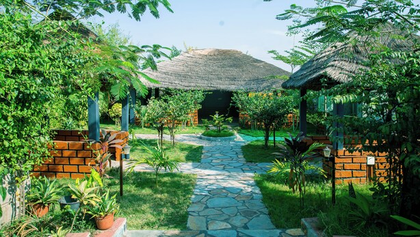 A garden pathway leading to a thatched-roof structure surrounded by greenery. - Aureza Paradise Hotel (Tamale)