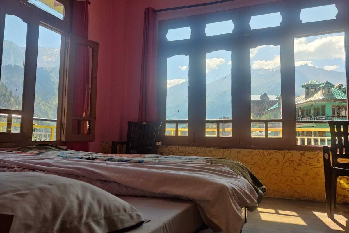 A room with a bed, a chair, and large windows with a mountain view.