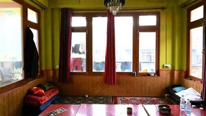 Una habitación con piso de madera, una mesa con una silla, una cama y una ventana con cortinas.