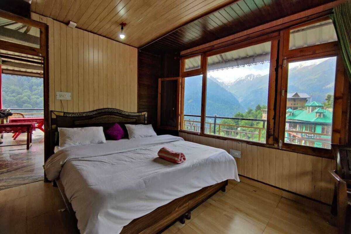 A wooden room with a bed, large windows, and a view of mountains.