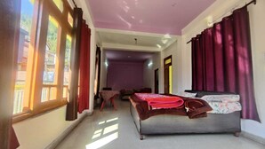 Una habitación con cama, una mesa y una silla. Hay una ventana con cortinas y una puerta que da a otra habitación.