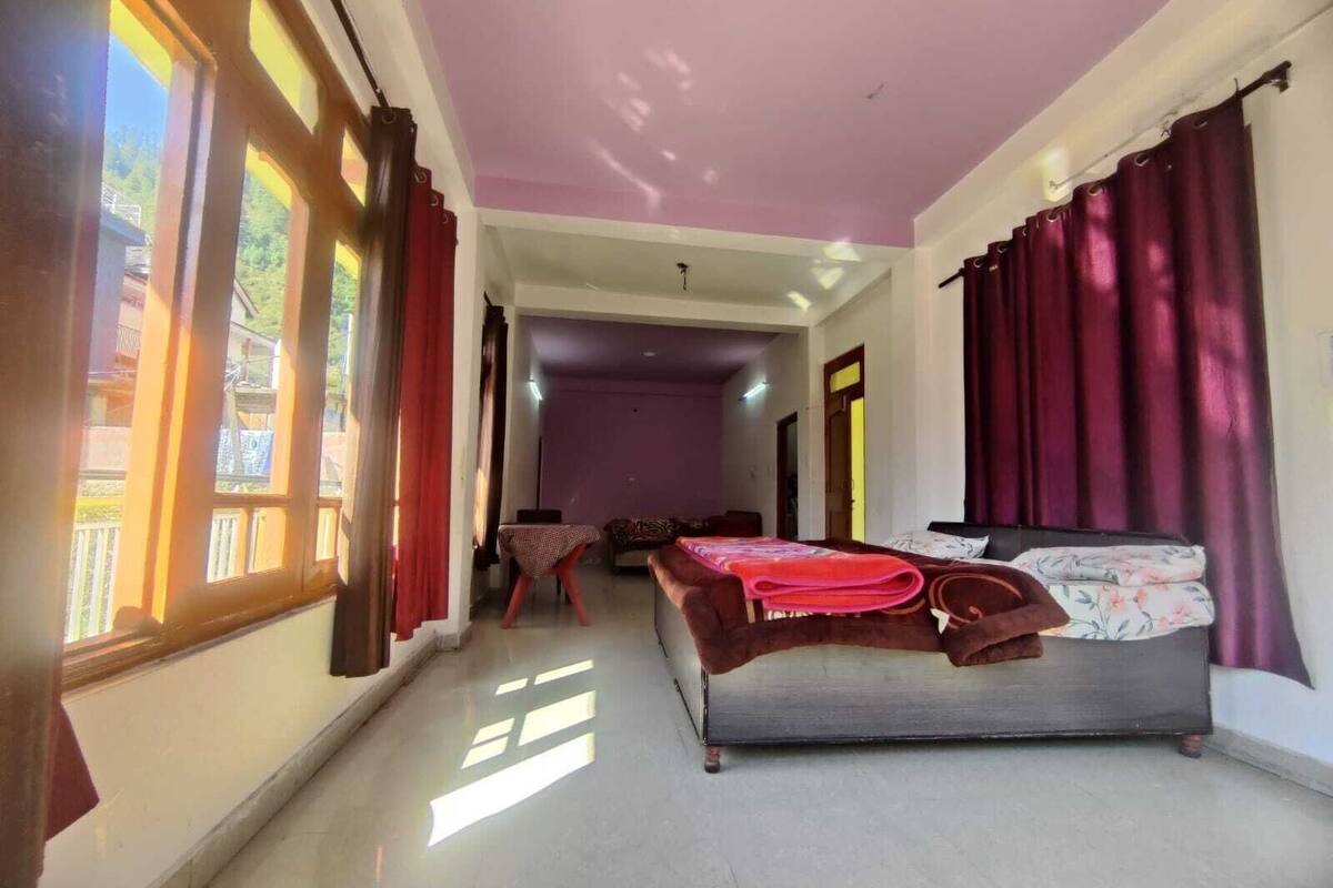 A room with a bed, a table, and a chair. There is a window with curtains, and a door leading to another room.