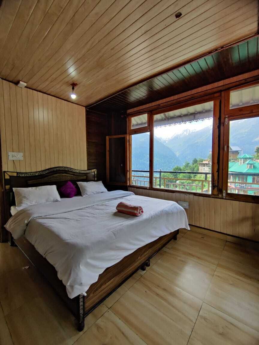 A wooden-paneled bedroom with a bed, large windows, and a view of mountains.