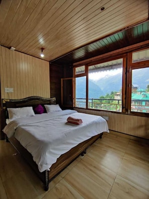 Un dormitorio con paneles de madera, una cama, ventanas amplias y vistas a las montañas.