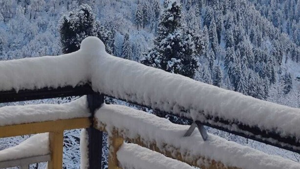 Eine verschneite Berglandschaft mit einem hölzernen Geländer im Vordergrund.