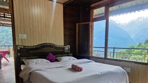 Una habitación de madera con una cama, un ventanal con vista a las montañas y un balcón.