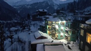 Un hotel con paisaje nevado, montañas al fondo y un edificio de varios pisos con ventanas iluminadas.