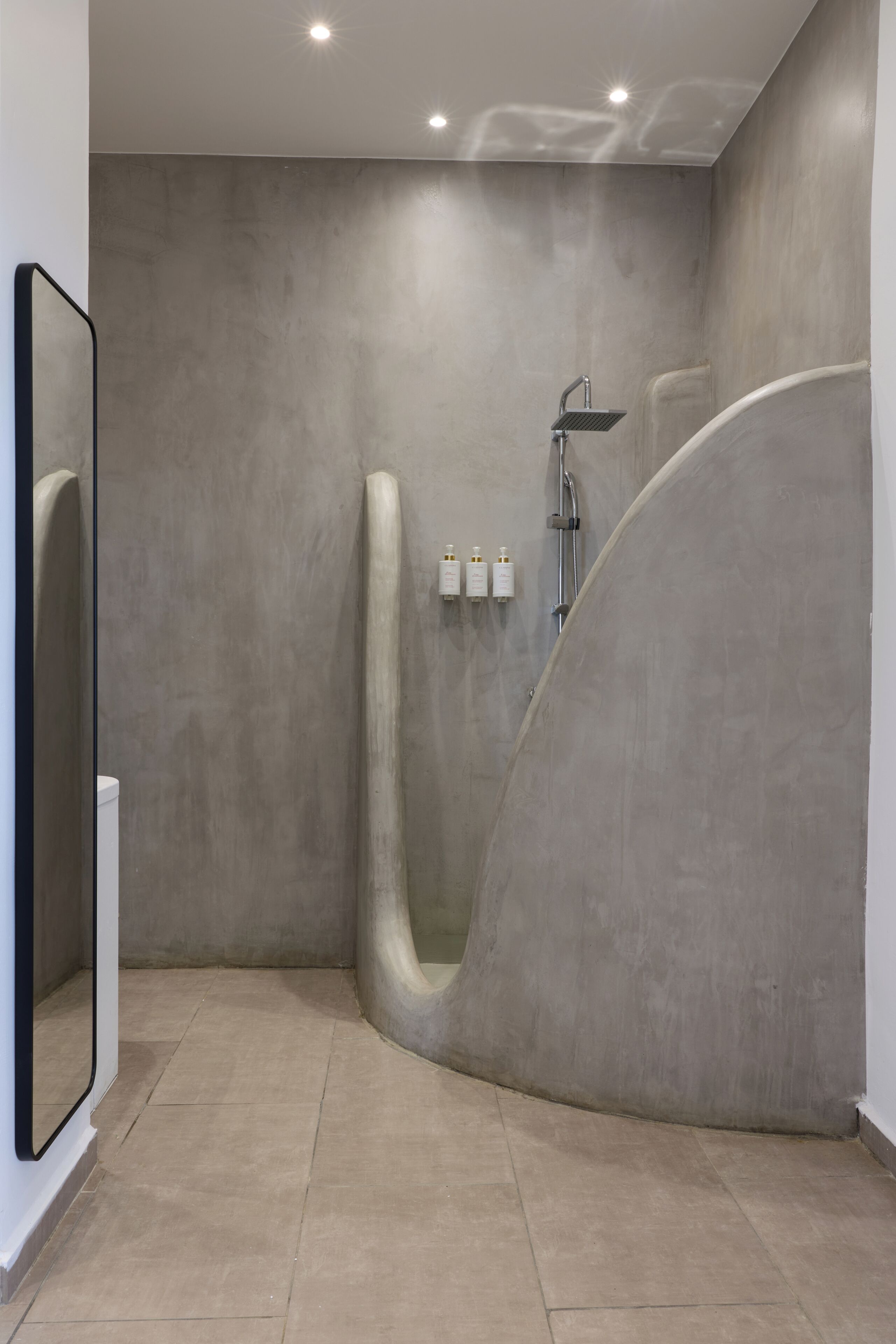 Een moderne badkamer met een gebogen douche, een grote spiegel en een zeepdispenser aan de muur.