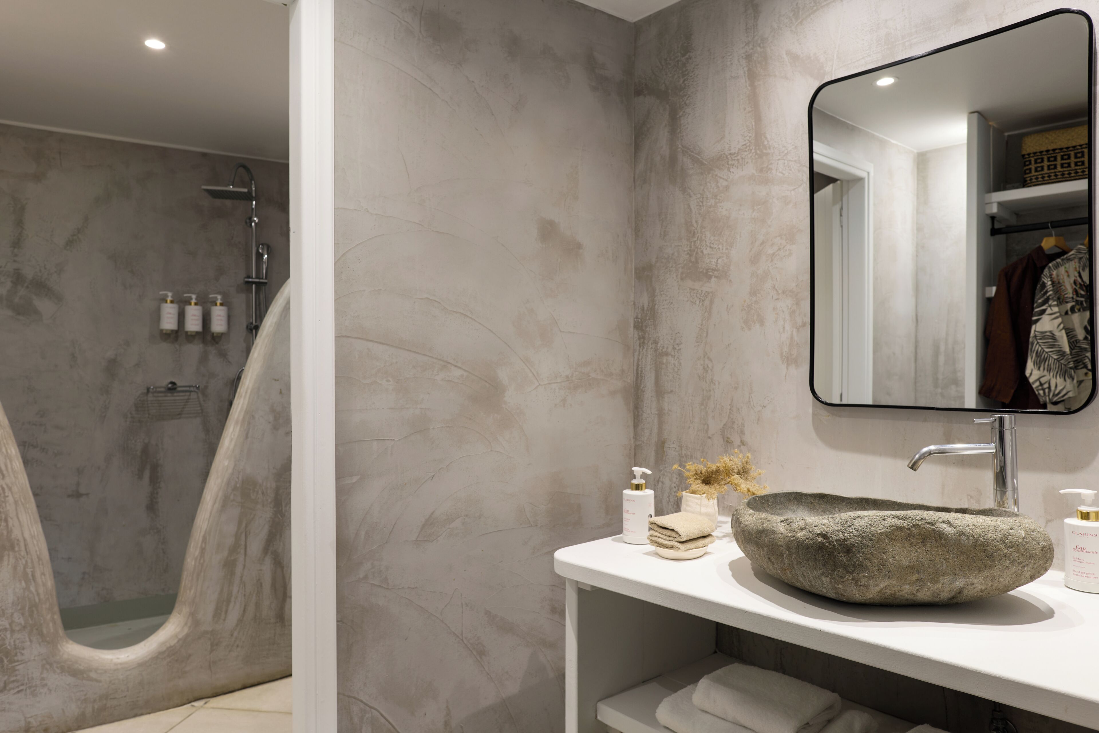 A modern bathroom with a freestanding bathtub, a round stone sink, and a large mirror.