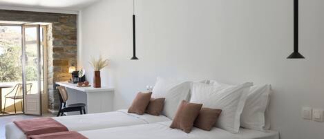 A modern bedroom with a large bed, a small desk, and a view through an open door.