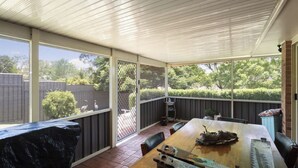 A covered patio with a wooden table, chairs, and a grill. - Modern 4BR Muswellbrook Stay (Muswellbrook)