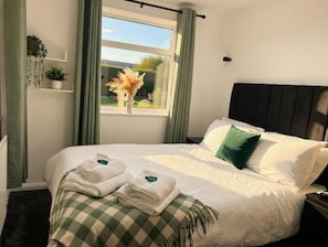 Una cama bien hecha con almohadas, una manta a cuadros y toallas dobladas.