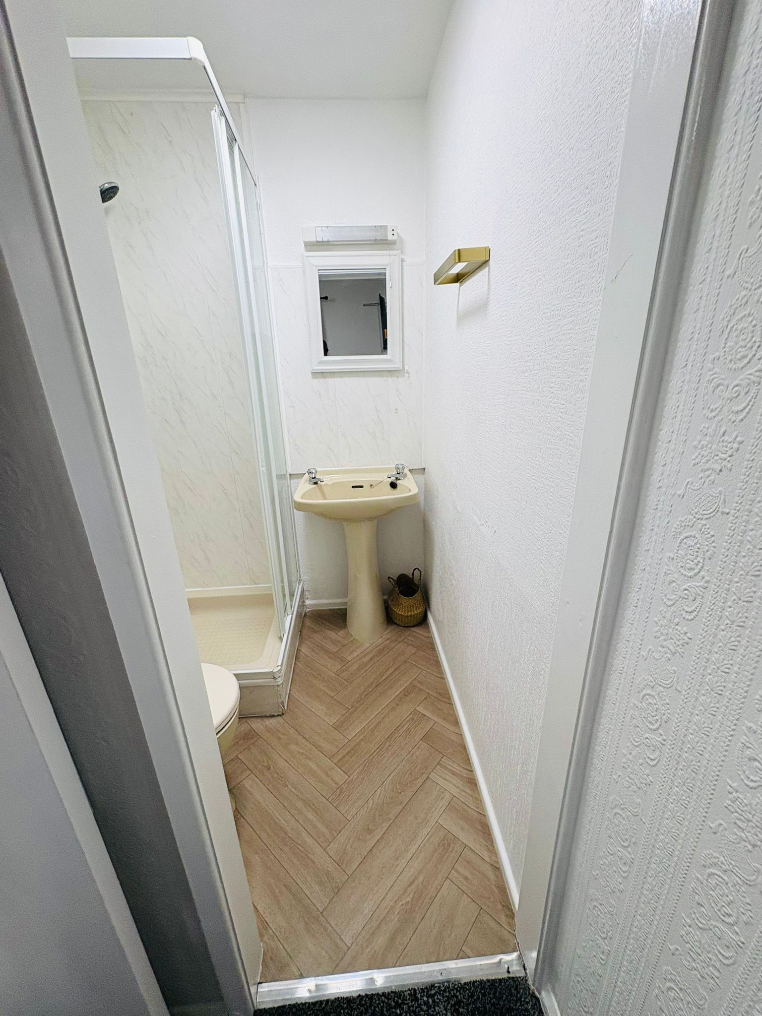 A narrow bathroom with a shower, toilet, and sink.