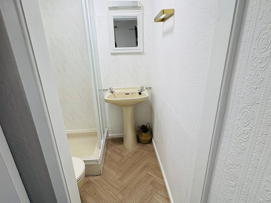 A narrow bathroom with a shower, toilet, and sink.