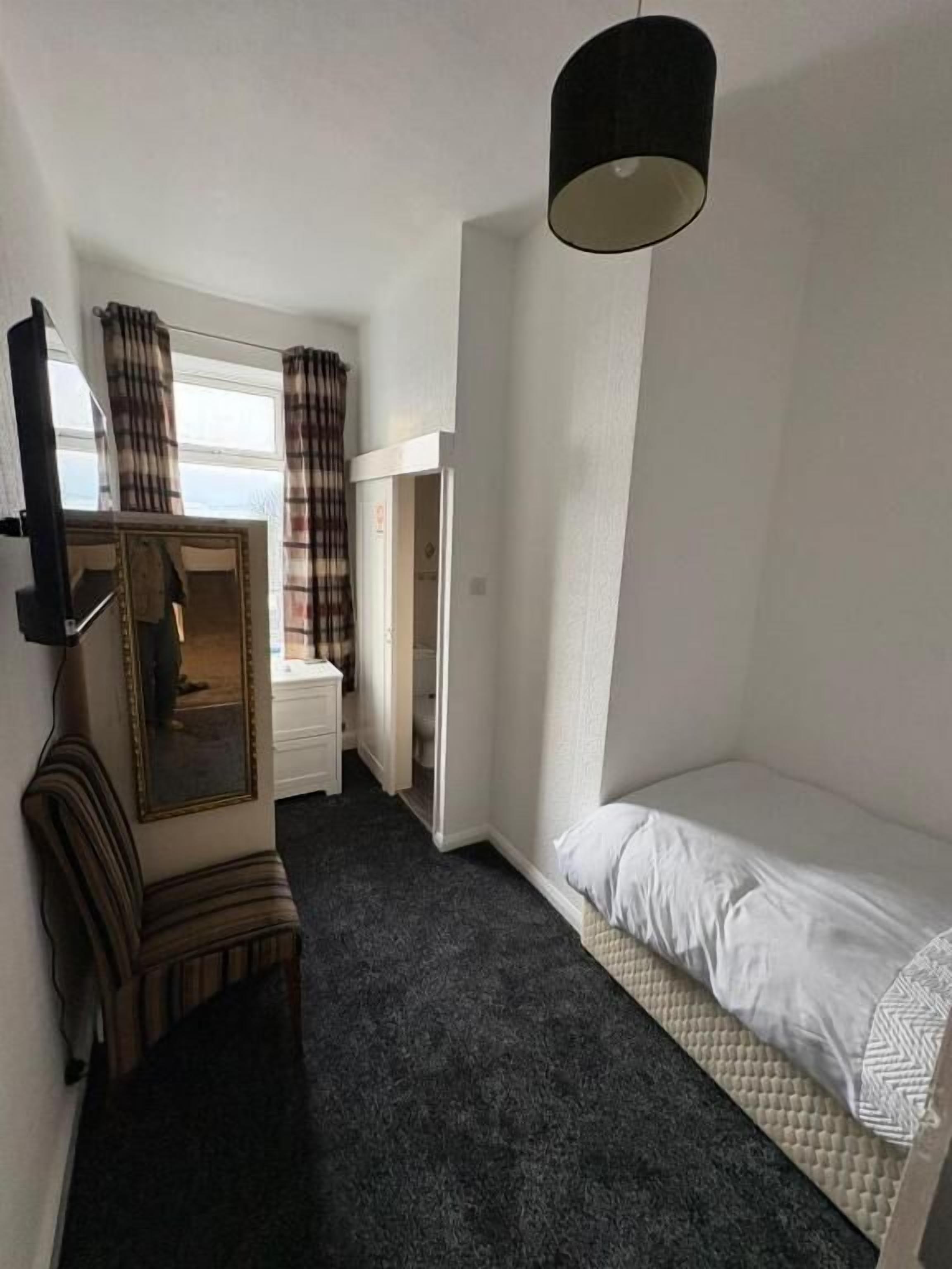 A small, single-bed room with a mirror, a wardrobe, a desk, and a hanging lamp.