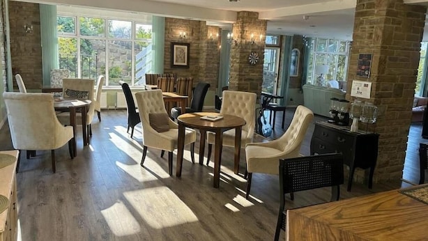 A spacious room with a large window, a stone pillar, and a dining area with chairs and a table.