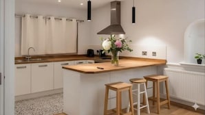 A modern kitchen with a central island, bar stools, pendant lights, and a flower vase.