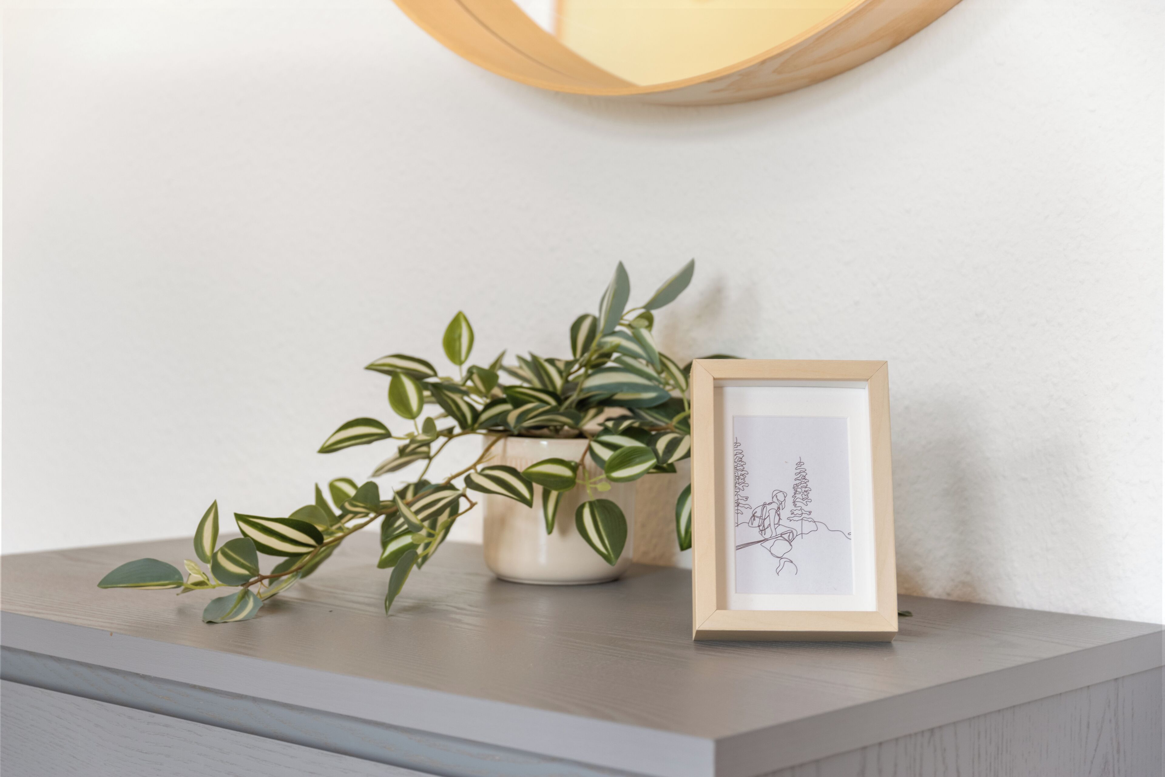 A framed artwork on a shelf, a potted plant, and a round wall light.