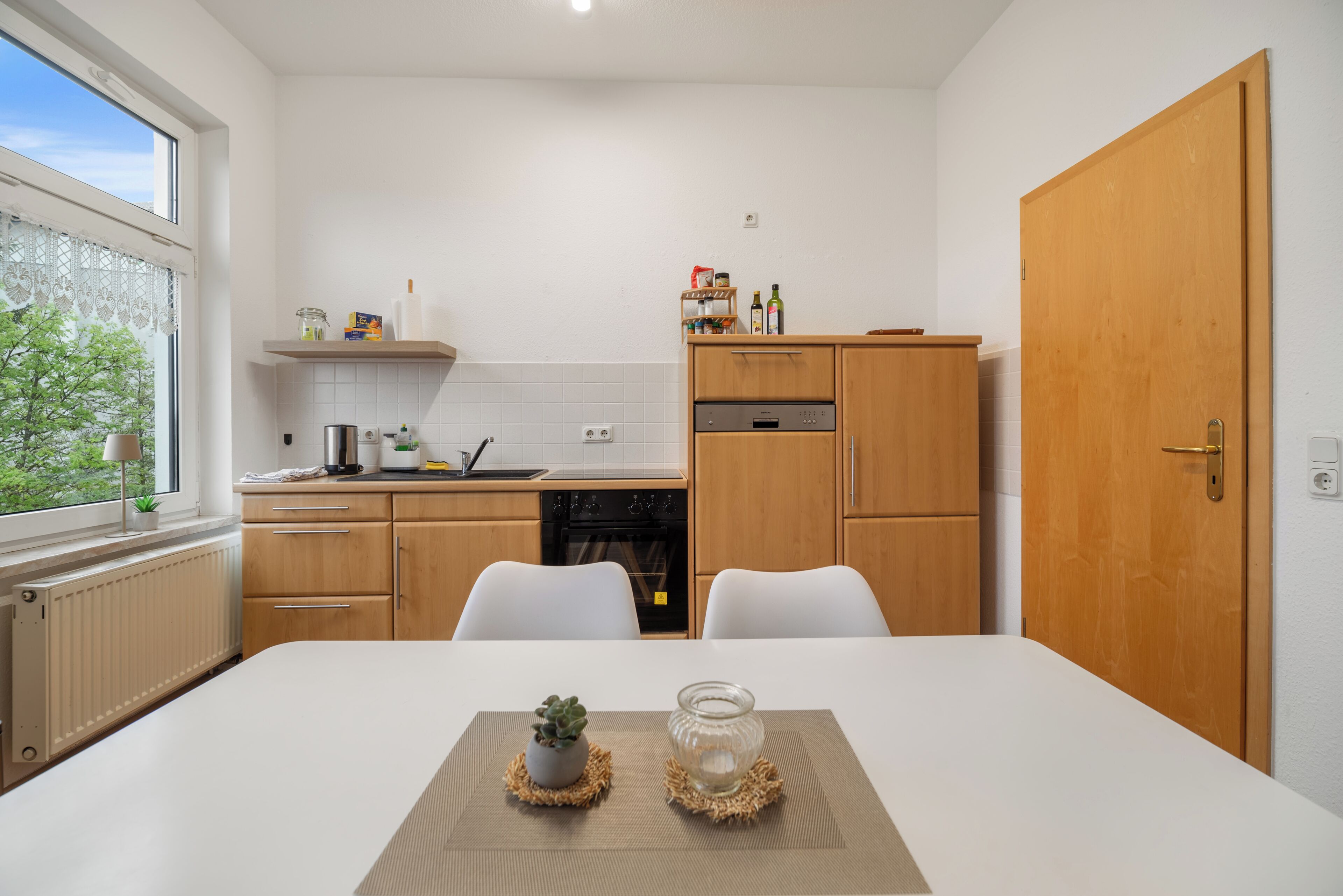 Cocina moderna con armarios blancos, una mesa de comedor con dos sillas y vistas al exterior.