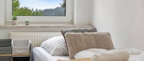 A bedroom with a bed, pillows, a window with a view of trees, and storage bins.