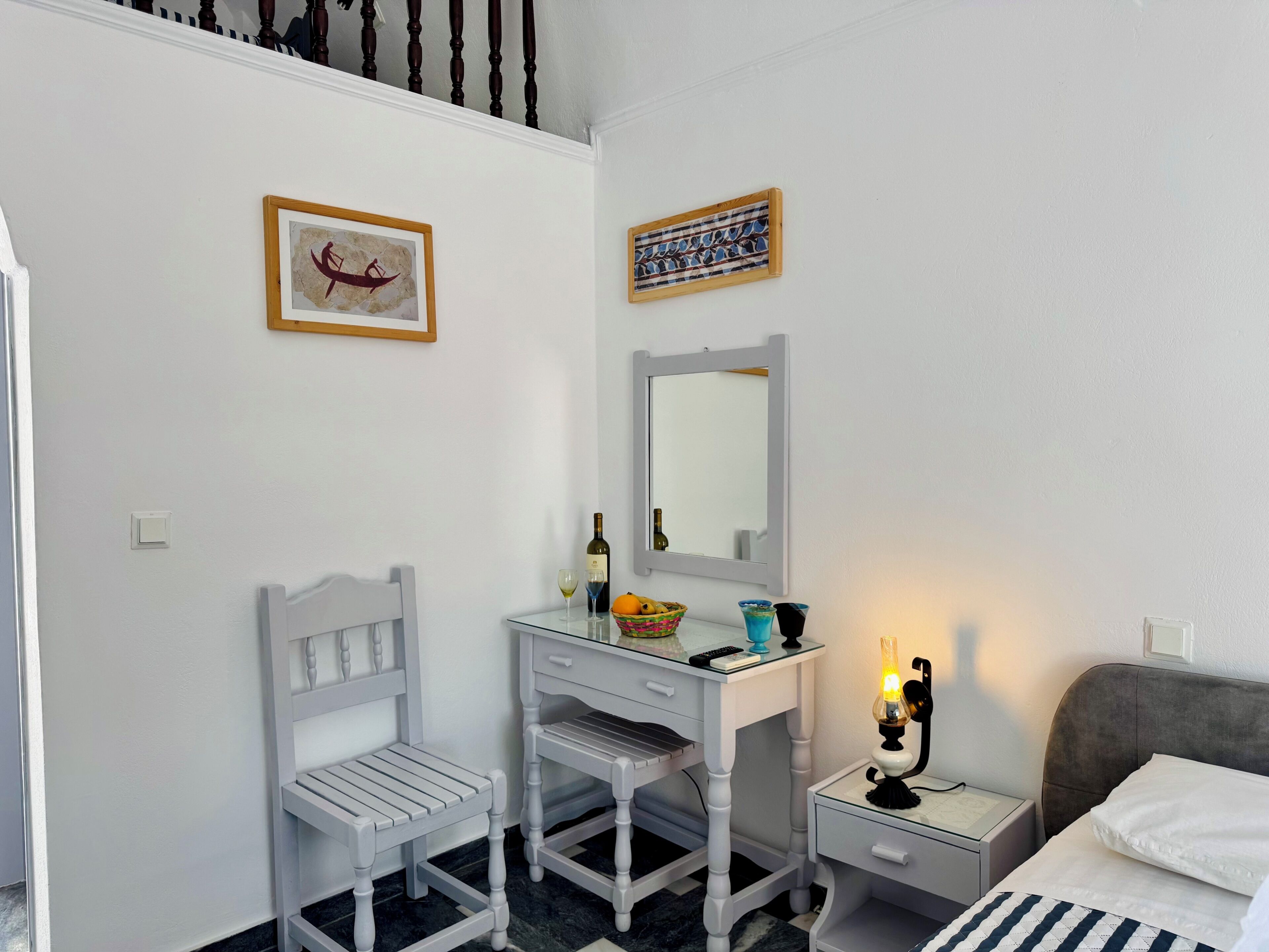 A bedroom with a bed, a desk with a chair, a nightstand, a lamp, and two framed pictures on the wall.