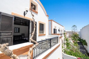 Un edificio blanco con balcones, barandilla negra y cielo azul despejado.