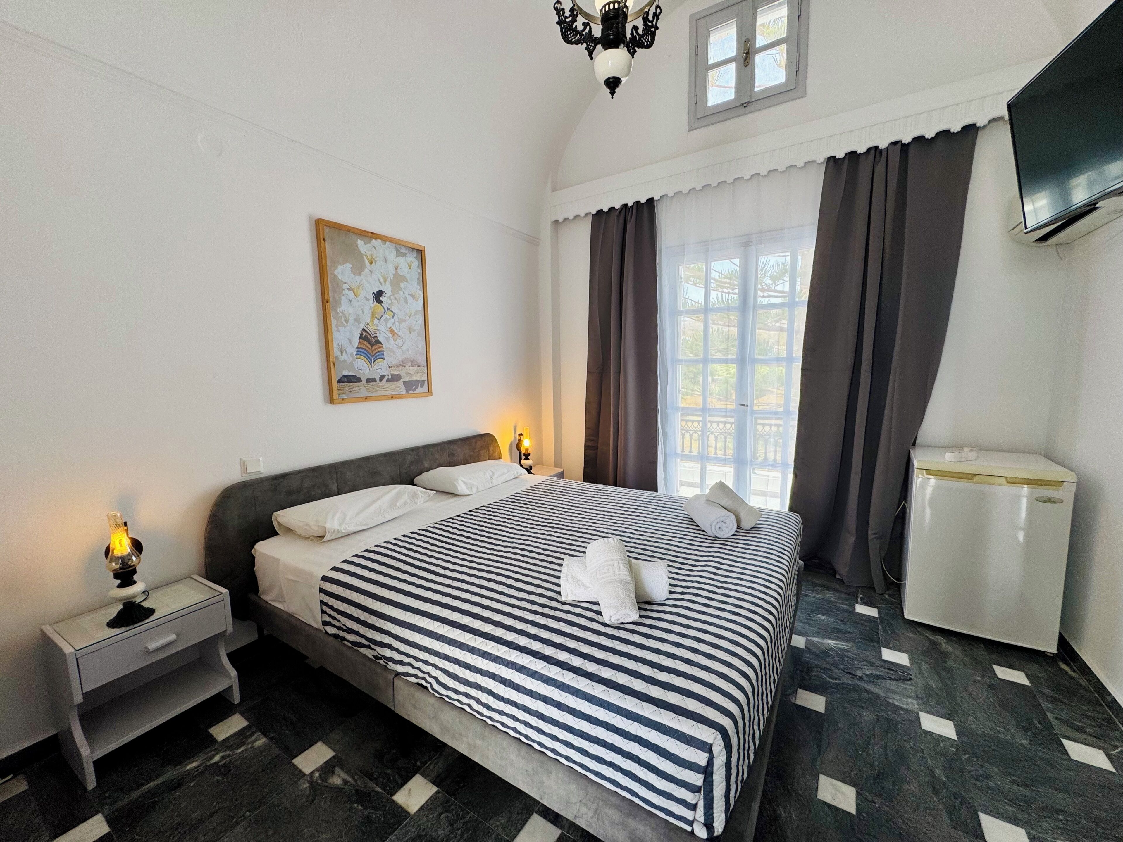 A hotel room with a bed, a nightstand, a painting, a window with curtains, and a television.