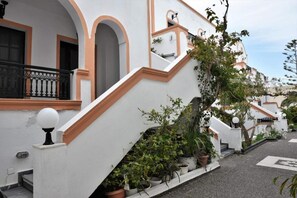 Um edifício branco com detalhes em laranja, uma escadaria e vasos de plantas.