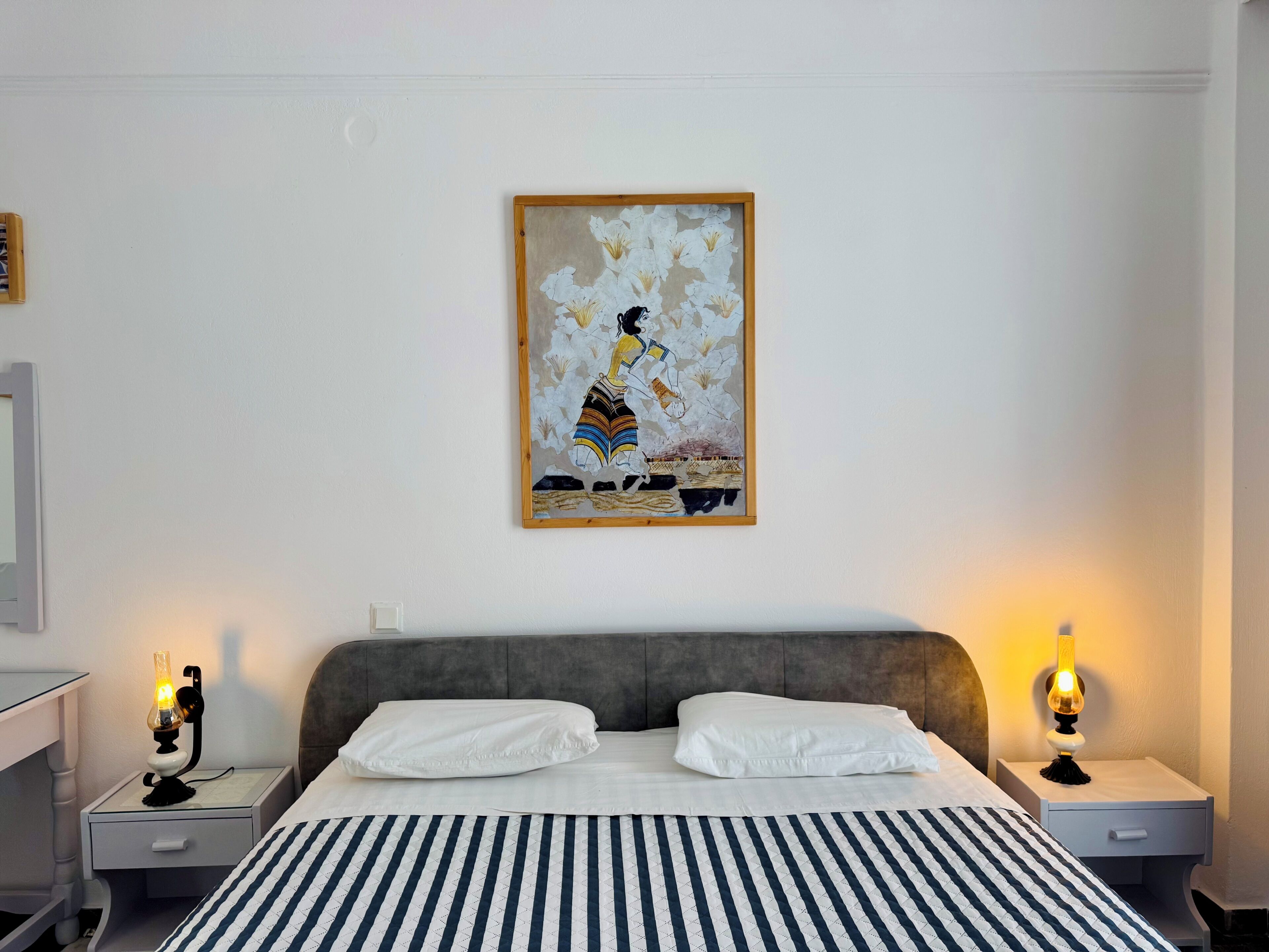 A bedroom with a bed, two bedside tables, a nightstand, a framed artwork on the wall, and two lit table lamps.