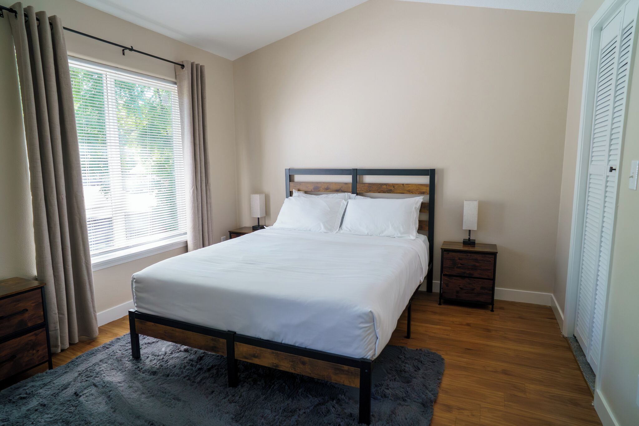Une chambre à coucher avec un lit, des tables de chevet, une fenêtre avec des rideaux et une porte.