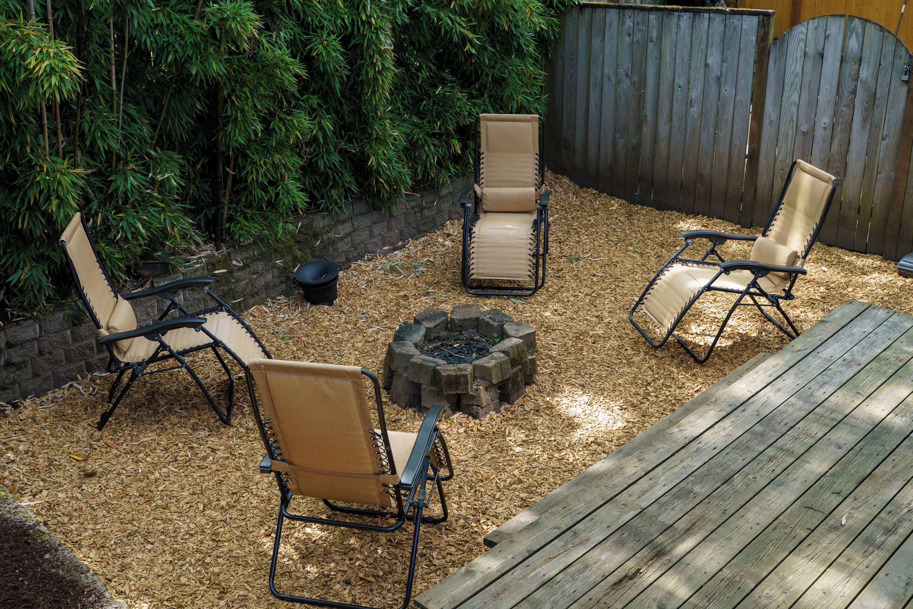 Une terrasse dotée de quatre chaises longues, d’un foyer extérieur et d’une clôture en bois.