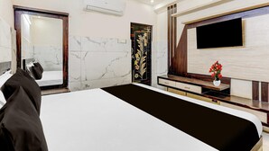 A modern hotel room with a large bed, a TV mounted on the wall, a wooden vanity, and a marble-tiled wall.