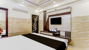 A hotel room with a large bed, a flat-screen TV mounted on the wall, a wooden cabinet, and a marble-patterned wall.