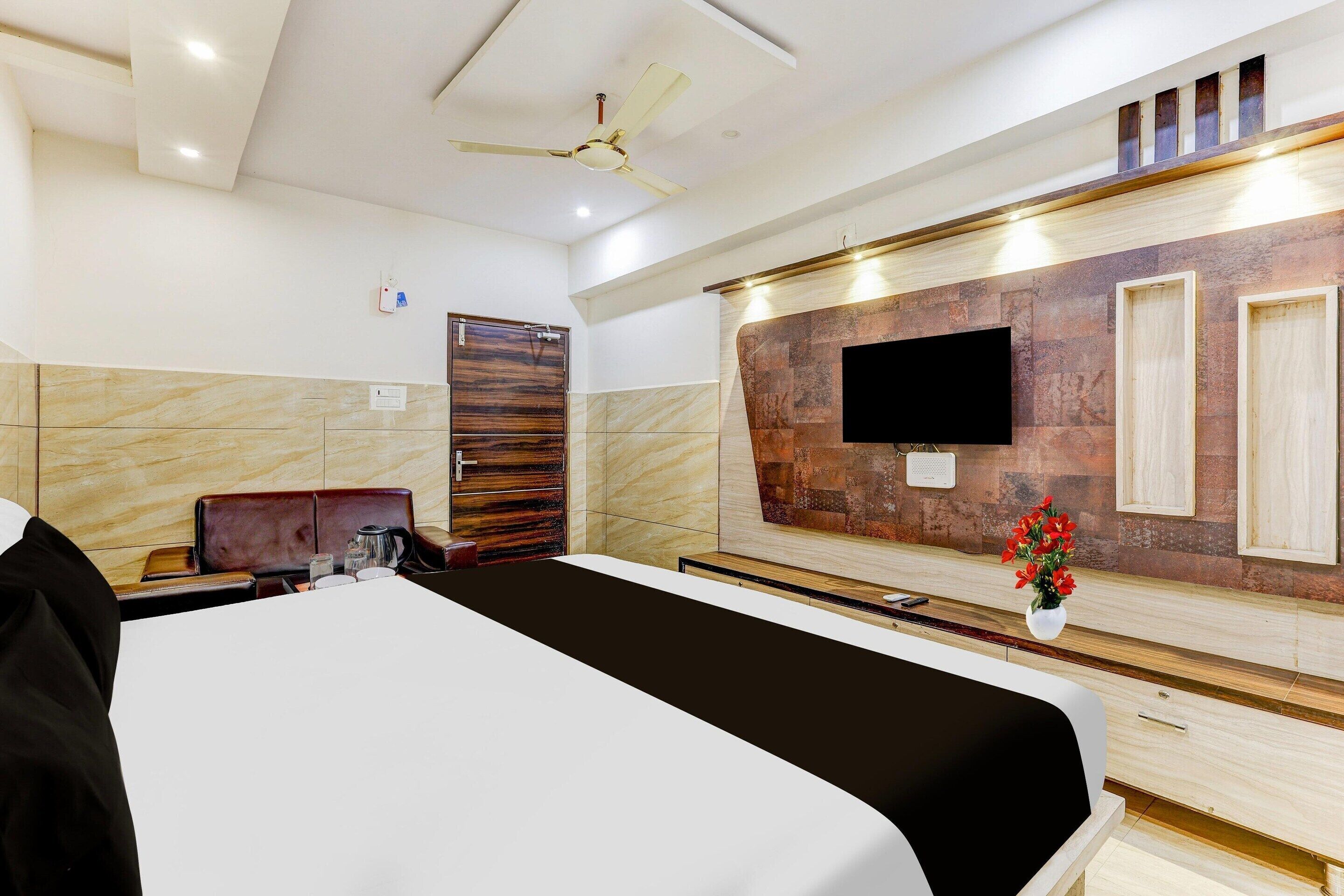 Habitación de hotel con cama, escritorio, silla, televisor montado en la pared y ventilador de techo.