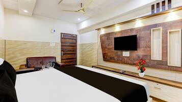 Habitación de hotel con cama, escritorio, silla, televisor montado en la pared y ventilador de techo.