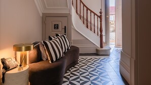 En gang med et geometrisk gulvmønster, en trappe, en sofa med stribede puder og en lampe med en telefon.