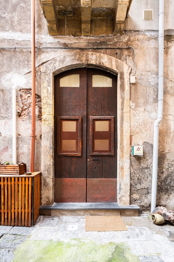 A rustic wooden door with a small window, a stone wall, and a metal pipe. - Ragione - City Center Apt by Wonderful Italy (Catania)