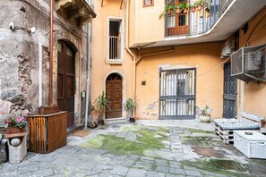 A courtyard with stone paving, wooden doors, potted plants, and outdoor furniture. - Ragione - City Center Apt by Wonderful Italy (Catania)