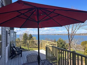 A deck with outdoor furniture, a red umbrella, and a view of a body of water.