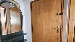 Une porte en bois avec une poignée en métal, un escalier en métal noir et un sol carrelé de carreaux blancs.