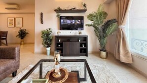 Een woonkamer met een televisie, bank, salontafel en potplanten.