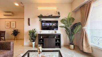 A living room with a TV, sofa, coffee table, and potted plants.